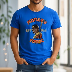 May include: Royal blue t-shirt featuring a graphic of a person with a staff, and the words "Monkey Magic" in gold and red. Chinese characters are also present. The shirt is short-sleeved.