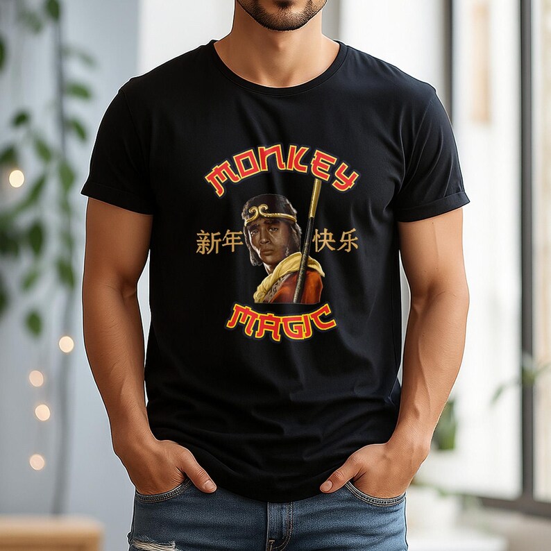 May include: Black t-shirt with a graphic featuring a portrait of a person with a staff, the words "MONKEY MAGIC" in red and gold, and Chinese characters. The shirt is short-sleeved.