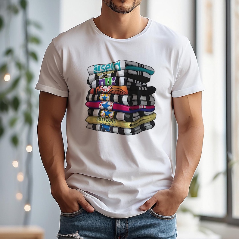 May include: White t-shirt featuring a stack of colorful scarves with various designs and text. The scarves are in shades of blue, black, yellow, pink, and orange. The text on the scarves includes the words "Kisel", "188", and "MCEWANS".