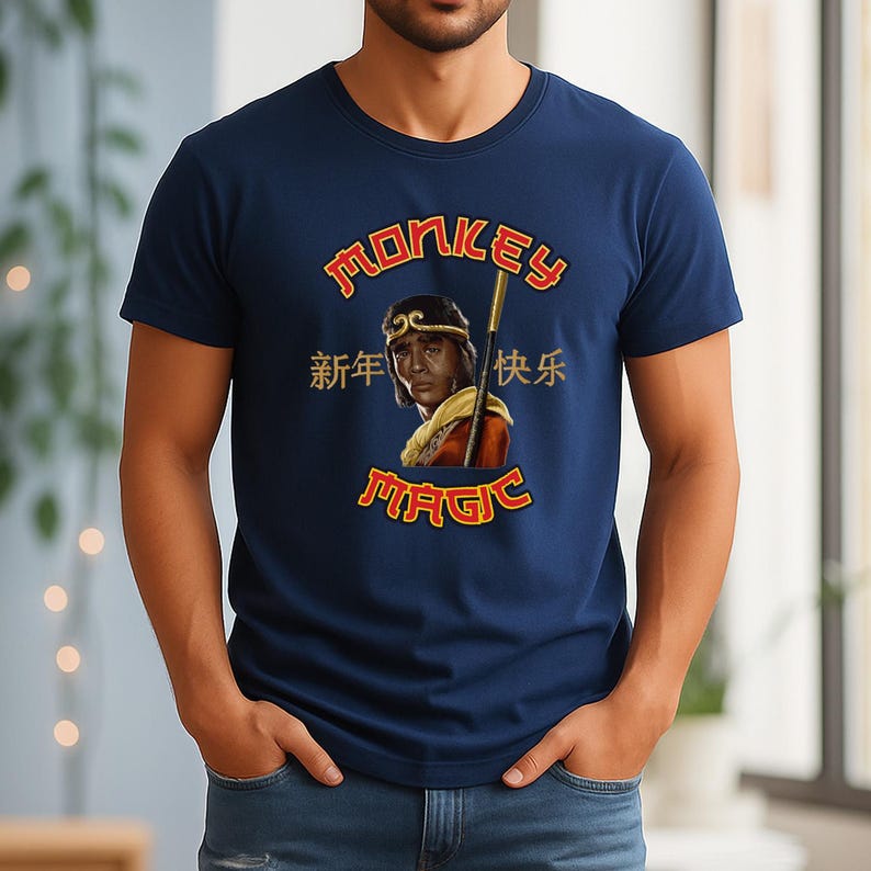 May include: Navy blue t-shirt featuring a graphic of a person with a staff, with the words "MONKEY MAGIC" in gold lettering. Chinese characters are also present. The shirt is a crew neck and made of a soft material.