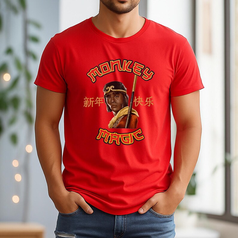 May include: Red t-shirt featuring a graphic of a person with a gold staff and the words "Monkey Magic" in gold lettering. Chinese characters are also present. The shirt is short-sleeved and has a crew neck.