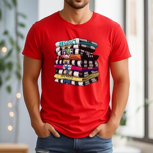 May include: A red t-shirt featuring a stack of colorful, folded items with text. The items are in various colors, including blue, black, yellow, and pink. The text on the items includes the word "ISELD" and "MCEWANS".