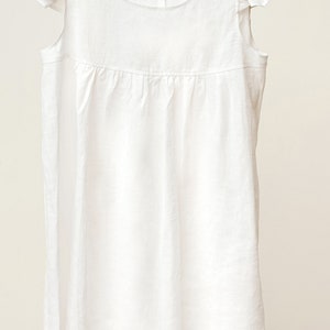 Puede incluir: Un vestido blanco de lino con mangas de volantes. El vestido tiene un escote redondo y una falda fruncida.