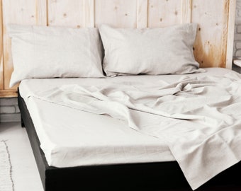 Puede incluir: Una sábana de cama de lino blanco con una cabecera de madera y dos almohadas de lino blanco. La sábana está ligeramente arrugada y las almohadas están dispuestas ordenadamente.