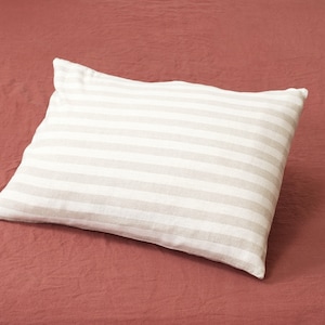 Puede incluir: Una almohada blanca con rayas grises sobre un fondo rojo.