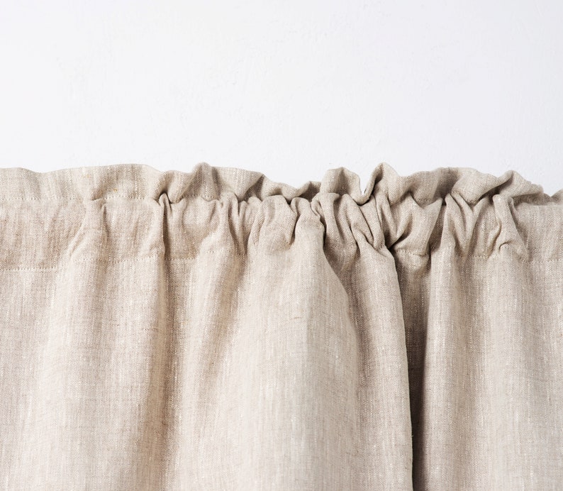 May include: A close-up of a beige linen curtain with a gathered top edge.