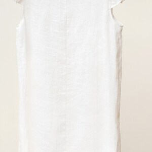 Puede incluir: Vestido blanco de lino con mangas de volantes. El vestido tiene un escote redondo y un corte holgado.