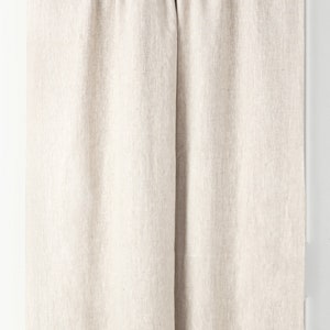 May include: A pair of off-white linen curtains hanging from a brown curtain rod. The curtains are gathered at the top and have a simple, natural look.