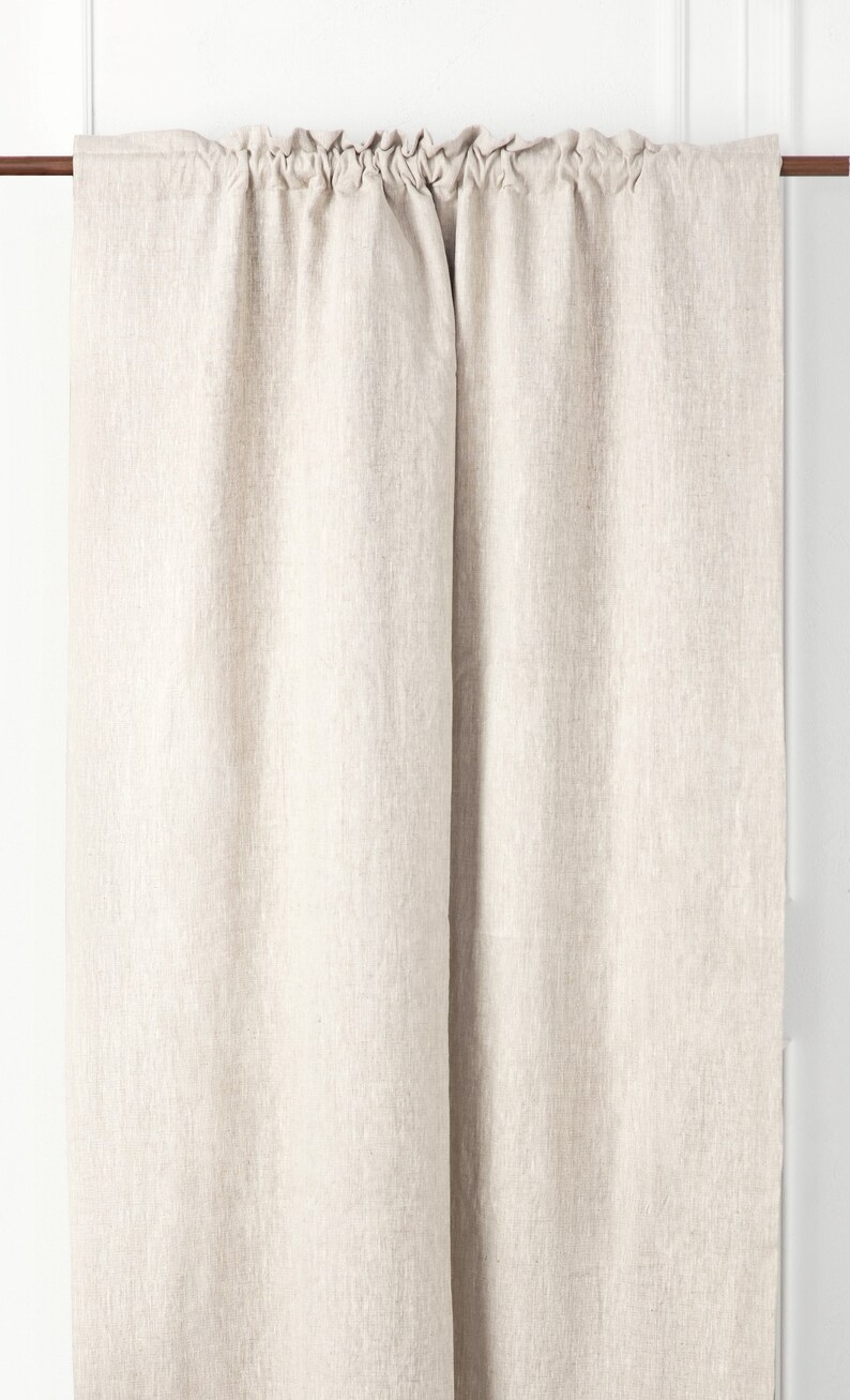 May include: A pair of off-white linen curtains hanging from a brown curtain rod. The curtains are gathered at the top and have a simple, natural look.