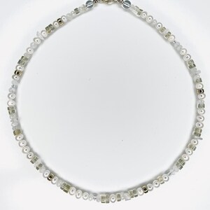 May include: A white and gold beaded necklace with a clasp fastening. The necklace features white pearls, gold beads, and clear square beads.