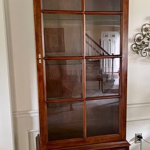 May include: A tall, dark wood cabinet with glass doors and two drawers. The cabinet has a curved top and brass hardware.