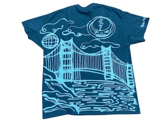 Könnte beinhalten: Dunkelblaues T-Shirt mit hellblauer Grafik der Golden Gate Bridge, einem Steal Your Face-Schädel und einem Globus. Das Shirt hat auch das Wort "Shuts" auf dem Ärmel. Das Design ist im handgezeichneten Stil.