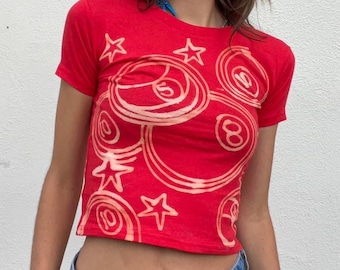 Könnte beinhalten: Rotes, bauchfreies T-Shirt mit einem weißen Design aus Billardkugeln und Sternen.