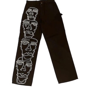 May include: Black carpenter pants with a white line drawing of four faces down the left leg.