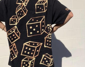 Könnte beinhalten: Schwarzes T-Shirt mit einem grafischen Druck von Würfeln in einem bräunlichen Farbton. Die Würfel sind über das T-Shirt verteilt.