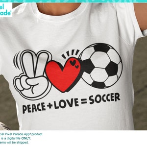 May include: White t-shirt with a black and white graphic design featuring a peace sign, a red heart, and a soccer ball. The text "PEACE + LOVE = SOCCER" is printed below the graphic.