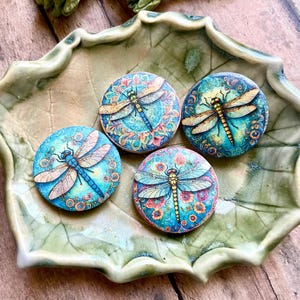 May include: Four round wooden ornaments with colorful dragonfly designs. Each ornament features a different dragonfly with intricate details and a floral background.
