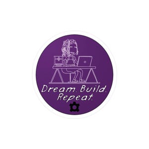 May include: Purple circle sticker with a white outline. The sticker features a cartoon illustration of a person sitting at a desk with a laptop and a box. The text "Dream. Build. Repeat." is written in white below the illustration. A small gear icon is in the center of the sticker.