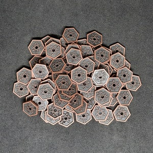 Könnte beinhalten: Eine Sammlung von kupferfarbenen Metallmarken mit einem Atom-Symbol-Design. Die Marken sind in einem Kreis auf einer grauen Oberfläche angeordnet.