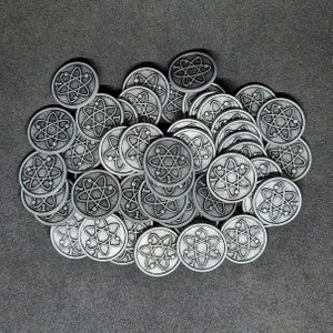 Pode incluir: Um monte de fichas de metal prateadas com um design de símbolo atômico. Cada ficha tem um design em relevo de um átomo com um círculo no centro.