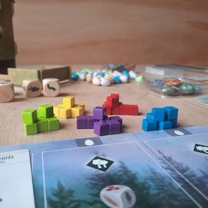 May include: A game board with colorful wooden blocks stacked in different patterns. The blocks are red, green, yellow, blue, and purple. The board has a light blue background with a forest scene.