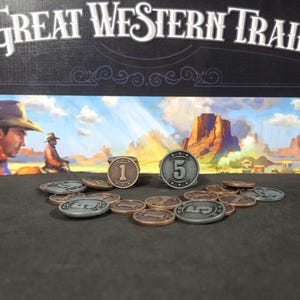 Op de afbeelding: Een close-up van een set metalen speltokens voor het bordspel Great Western Trail. De tokens zijn zilver en koperkleurig en hebben de nummers 1 en 5.