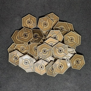 Puede incluir: Un montón de fichas de metal de color dorado con el número "10" impreso en cada una. Las fichas tienen forma de estrella de seis puntas.