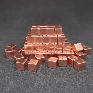 May include: A pyramid of small, copper-coloured cubes. The cubes are arranged in a pyramid shape, with the largest cube at the bottom and the smallest cube at the top. There are also several smaller cubes scattered around the base of the pyramid.