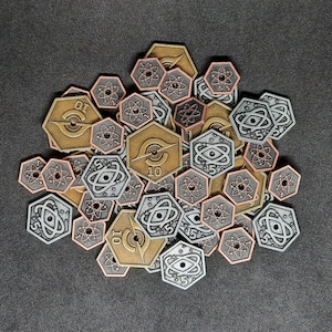May include: A collection of silver and copper tokens with various designs, including numbers, symbols, and geometric patterns. The tokens are arranged in a circular pattern on a dark grey surface.