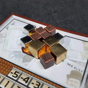 Peut inclure: Un groupe de petits cubes métalliques aux tons argent, or et cuivre sont disposés en forme de pyramide. Les cubes sont empilés les uns sur les autres, créant un design tridimensionnel.
