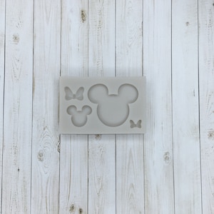 May include: A silicone mold with three cutouts: a large Mickey Mouse head, a smaller Mickey Mouse head, and a bow.