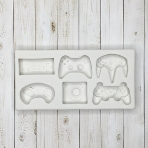 May include: White silicone mold with six different video game controller designs. The mold includes a classic NES controller, a Sega Genesis controller, a Playstation controller, an Xbox controller, a Nintendo Switch controller, and a generic joystick.