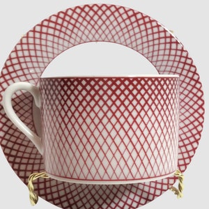 May include: A white teacup and saucer set with a red and white geometric pattern. The cup and saucer have a diamond pattern.
