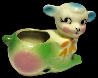 Peut inclure: Un pot en céramique en forme d'agneau vert et blanc avec une tête bleue et un nœud jaune. Le pot a une tache rose sur le côté et une petite ouverture dans le dos pour planter.