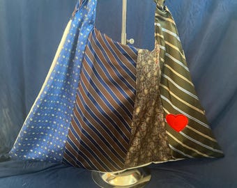 Può includere: Una grande borsa tote realizzata con cravatte riutilizzate. La borsa è composta da cinque cravatte con diversi motivi, tra cui blu con palme bianche, strisce marroni e blu, paisley marrone e bianco e strisce verdi e blu. Un cuore rosso è cucito sulla parte anteriore della borsa.