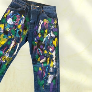 Pu&ograve; includere: Jeans di denim blu scuro con un colorato design astratto a spruzzi di vernice. La vernice comprende giallo, viola, bianco, verde e nero. I jeans hanno un classico design a cinque tasche.