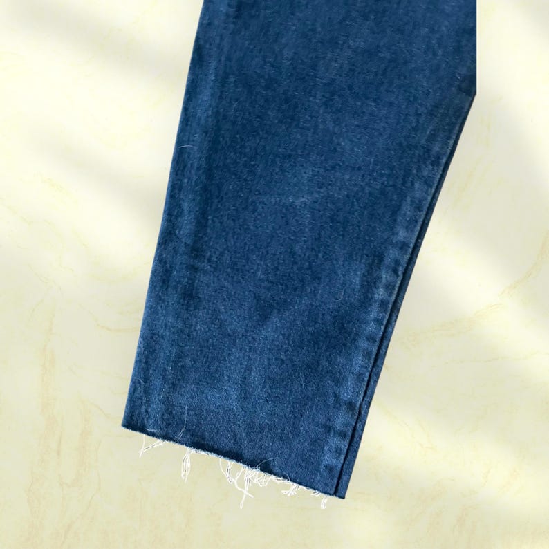 Pu&ograve; includere: Primo piano di una sezione di jeans blu. L'orlo &egrave; sfilacciato con fili bianchi. Il tessuto ha un aspetto strutturato ed &egrave; di una tonalit&agrave; media di blu.