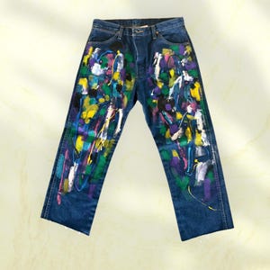 Pu&ograve; includere: Jeans di denim blu scuro con un vivace design astratto a spruzzi di vernice. La vernice comprende bianco, giallo, viola, verde e nero. I jeans hanno un classico design a cinque tasche.