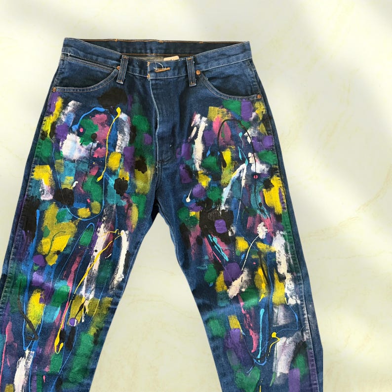 Pu&ograve; includere: Jeans di denim blu scuro con un design astratto e colorato a spruzzi di vernice. La vernice include giallo, verde, viola, rosa e bianco, creando un look unico e artistico. I jeans hanno un classico design a cinque tasche.