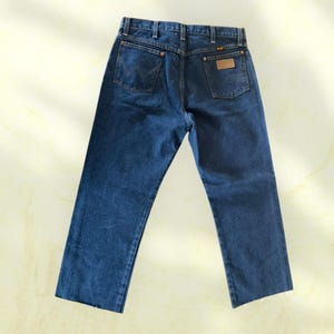 Pu&ograve; includere: Jeans di denim blu scuro con un classico design a cinque tasche. I jeans presentano l'etichetta del marchio Wrangler sulla tasca posteriore e un logo cucito sulle tasche posteriori. I jeans hanno un taglio dritto.