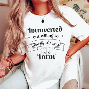 May include: White t-shirt with the text "Introverted but willing to briefly discuss Tarot" and a graphic of two tarot cards.