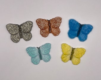 Peut inclure: Cinq embellissements en résine en forme de papillon pailletés dans différentes couleurs : argent, marron, bleu, bleu clair et jaune.
