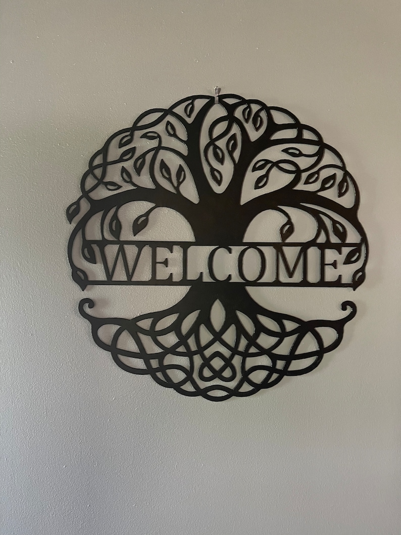 May include: Black metal wall decor featuring a tree of life design with intricate branches and roots. The word "WELCOME" is displayed across the center of the design.