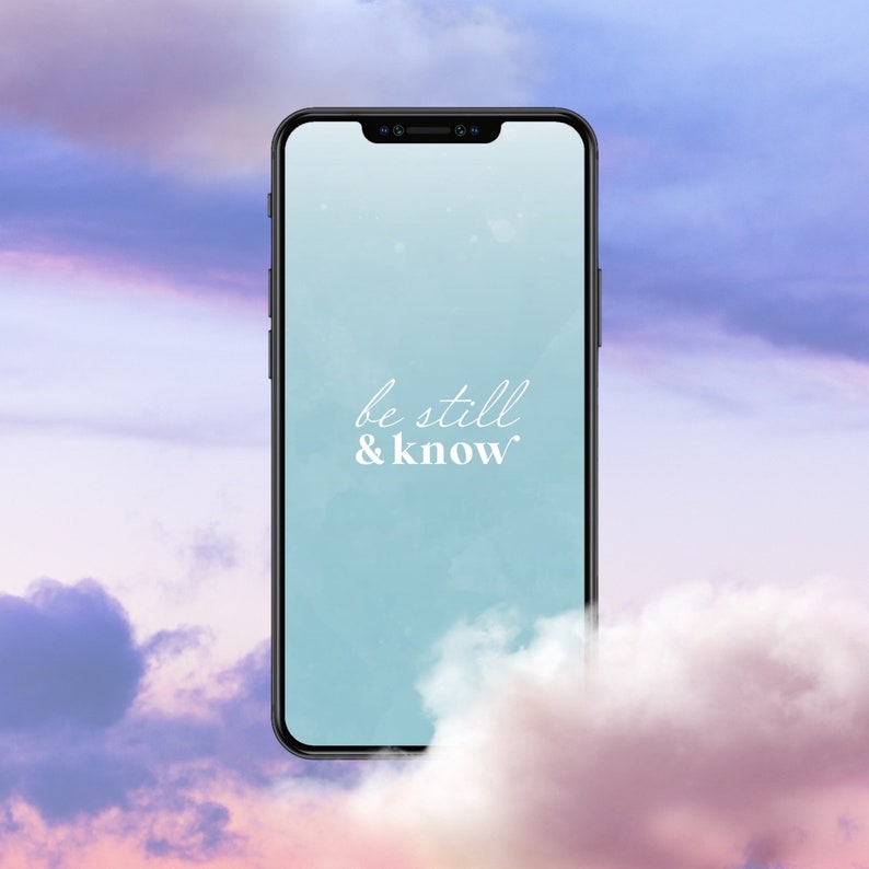 Op de afbeelding: Een smartphone met een blauwe achtergrond en de tekst "be still & know" op het scherm. De telefoon is omringd door wolken.