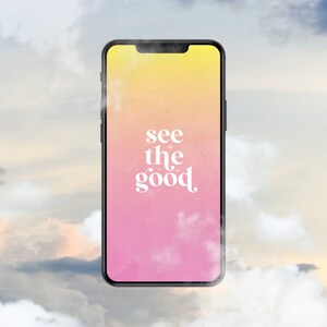 Op de afbeelding: Een smartphone met een roze en gele gradi&euml;nt achtergrond en de tekst "see the good" in wit. De telefoon staat voor een bewolkte lucht.