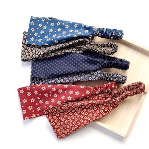 May include: Several floral print headbands in shades of blue, navy, black, and burgundy. Each headband has a repeating white flower design and an elasticated band. The headbands are presented on a wooden tray.