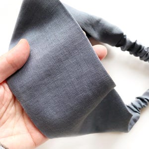 May include: A gray fabric headband with an elastic band. The headband is made of a soft, textured material and is designed to be worn around the head. The elastic band is a darker shade of gray.