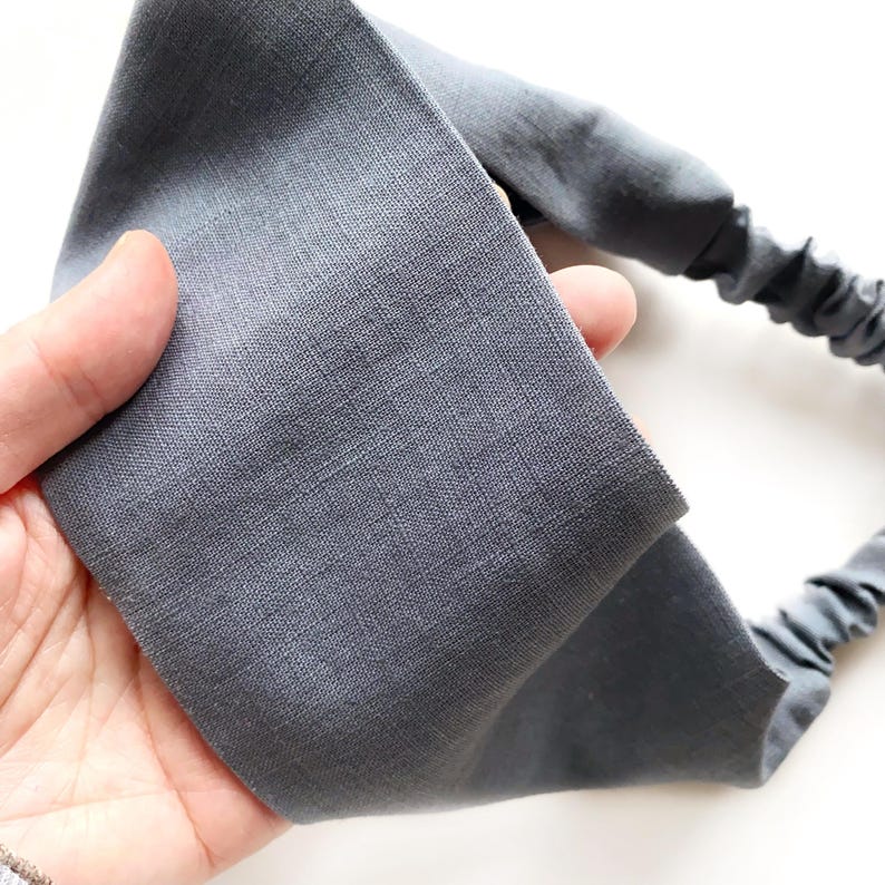 May include: A gray fabric headband with an elastic band. The headband is made of a soft, textured material and is designed to be worn around the head. The elastic band is a darker shade of gray.