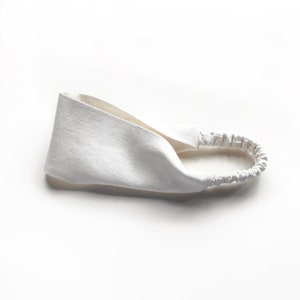 May include: A white headband with a textured fabric design. The headband features a wide, twisted front section and an elastic band at the back for a comfortable fit. This hair accessory is suitable for various hairstyles.