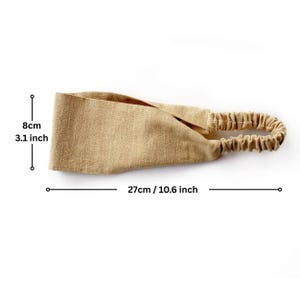 May include: A tan-colored headband with an elastic band. The headband is 10.6 inches long and 3.1 inches wide. The fabric has a textured appearance. The elastic band is gathered and has a similar tan color.